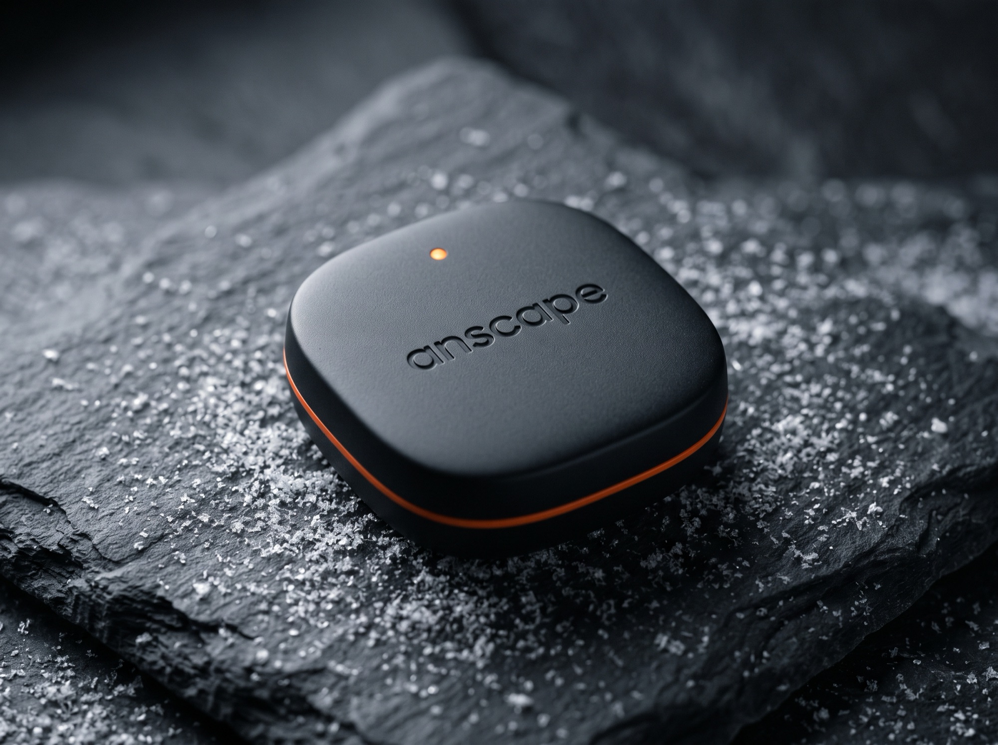 The anscape puck: a small matte-black rounded square with an orange ring and status light, resting on snowy slate